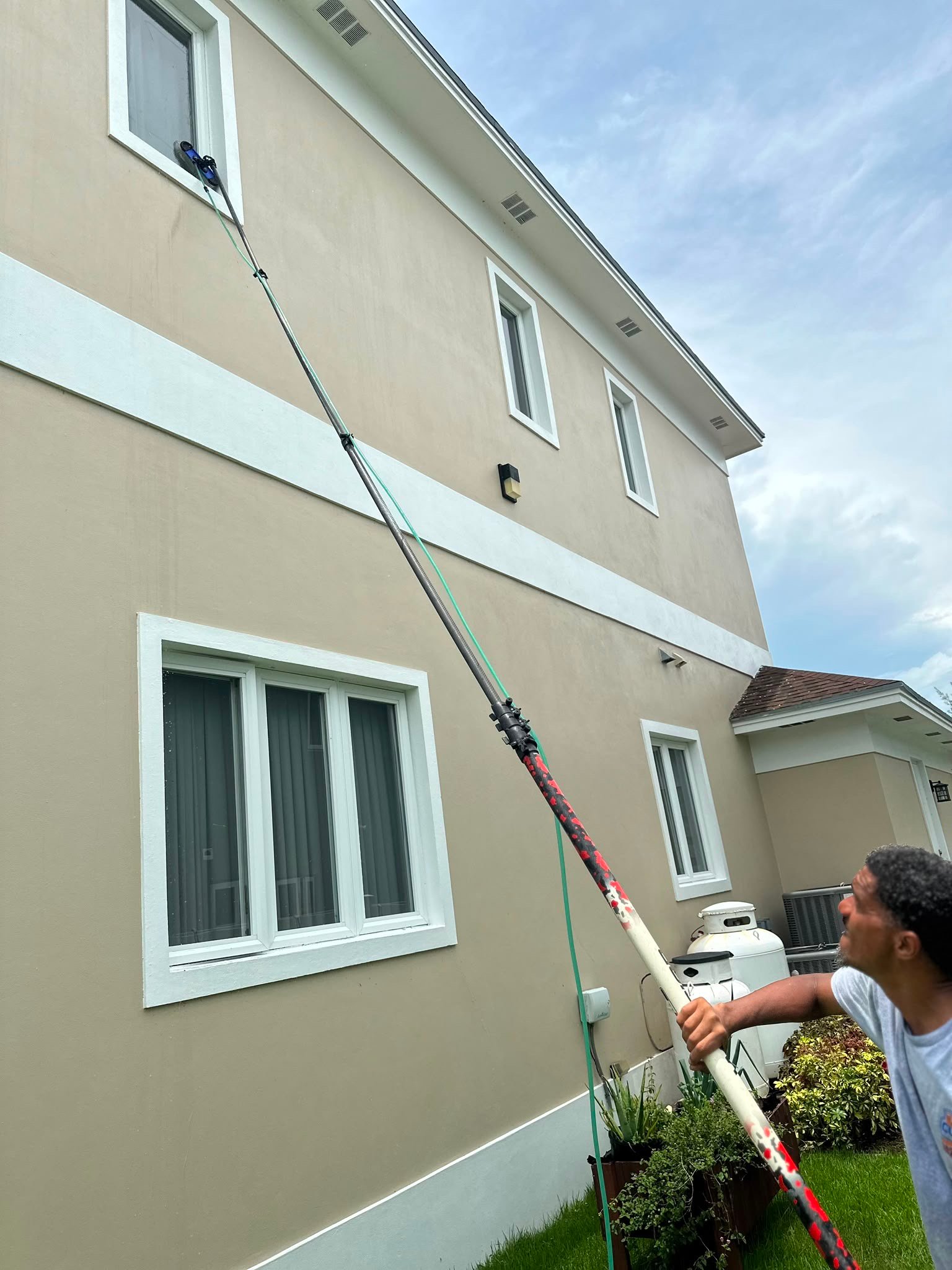 D.B. Clean242 technician cleaning second-story windows with a water-fed pole on a home in The Bahamas