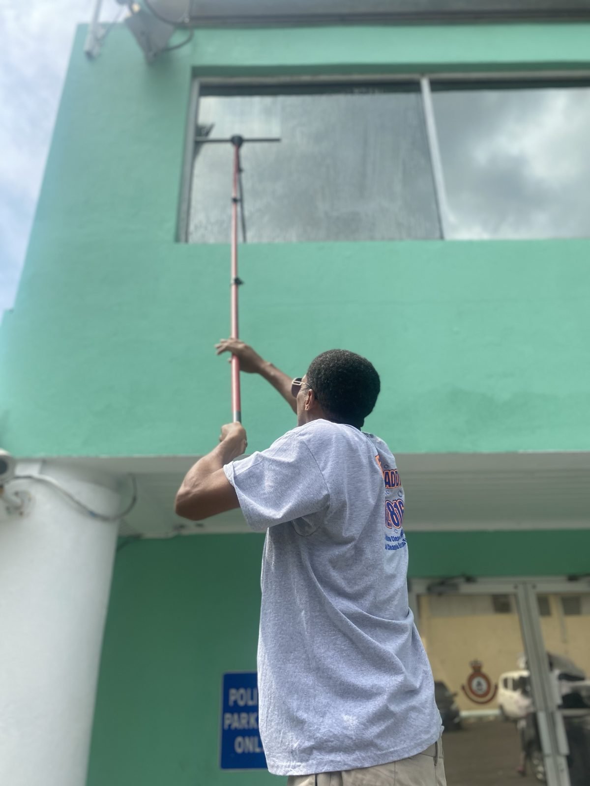 D.B. Clean242 technician using an extension pole and squeegee to clean a second-storey window from the ground