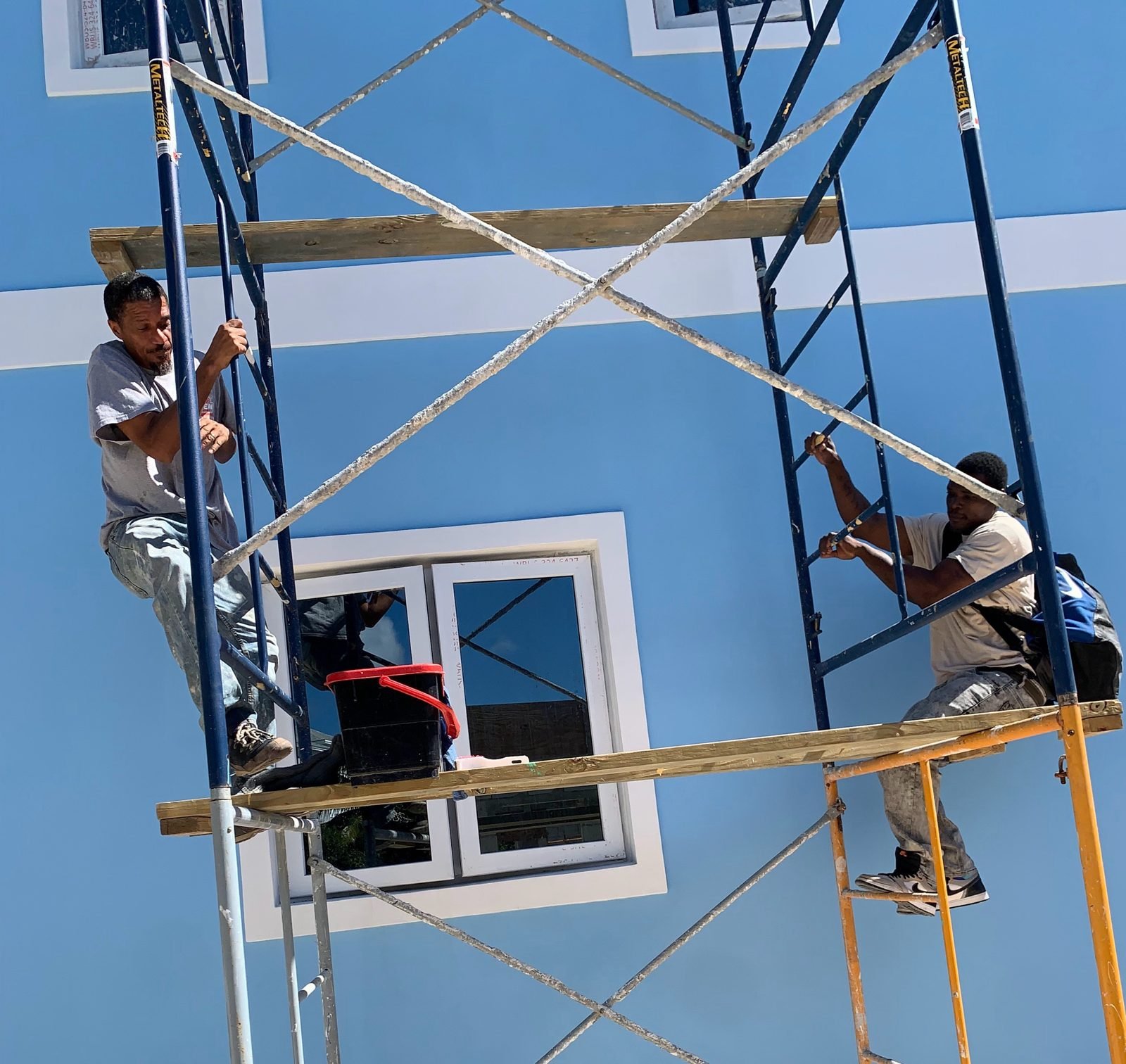 Two D.B. Clean242 technicians on scaffolding cleaning the windows of a blue commercial building